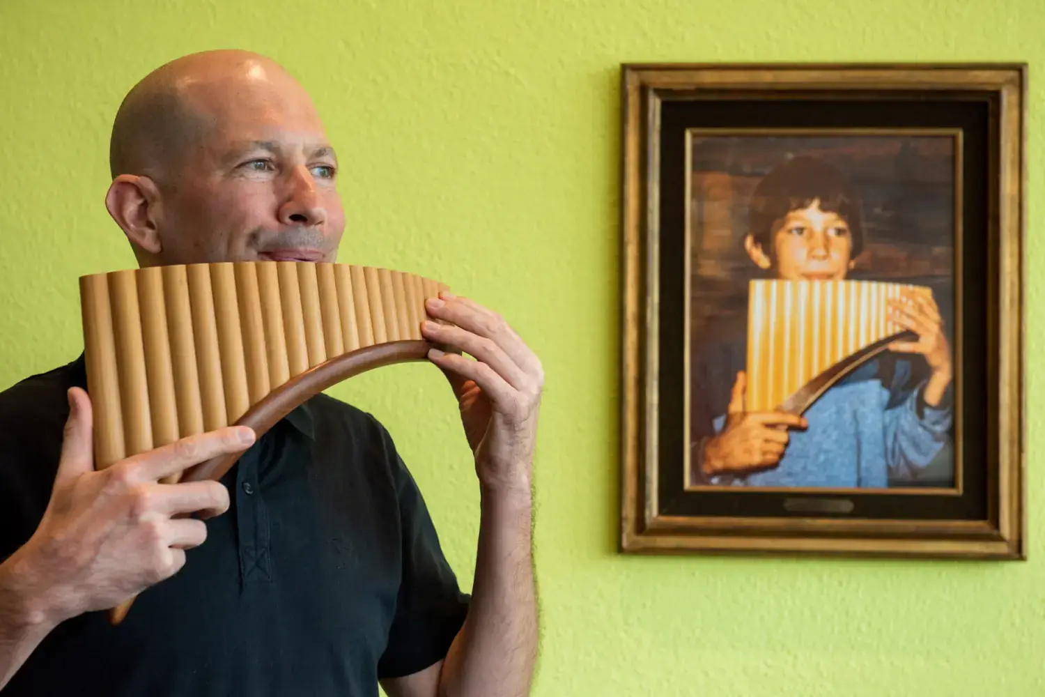 Michael Dinner spielt Panflöte; im Hintergrund ein Kinderfoto mit ihm in derselben Pose